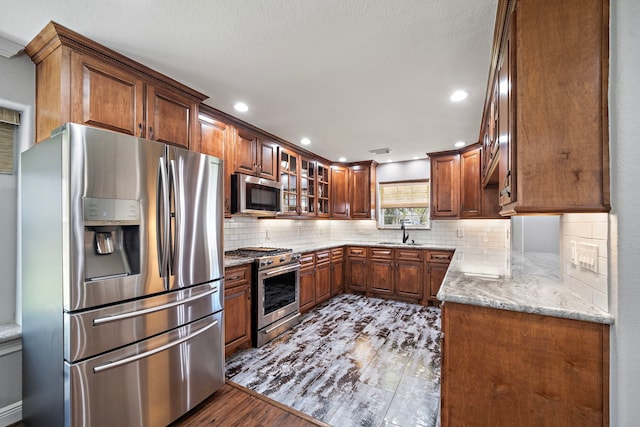 kitchen with light stone counters, stainless steel appliances, tasteful backsplash, glass insert cabinets, and a sink