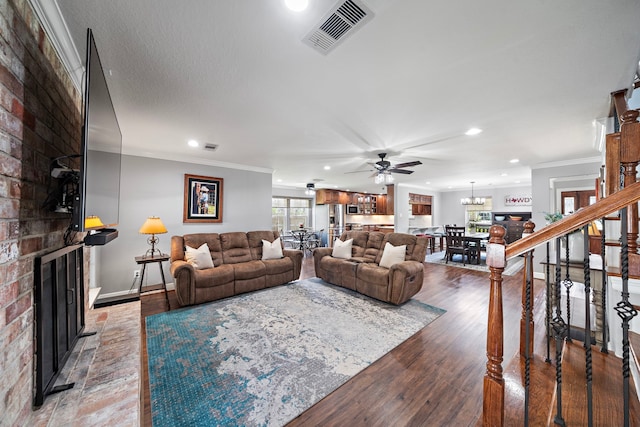 living area featuring wood finished floors, a ceiling fan, visible vents, a brick fireplace, and crown molding