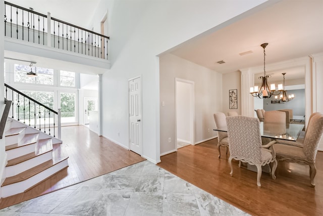 dining area featuring wood finished floors, a towering ceiling, baseboards, stairway, and an inviting chandelier