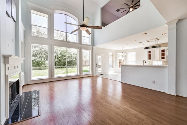 unfurnished living room featuring a towering ceiling, a high end fireplace, wood finished floors, and ceiling fan with notable chandelier