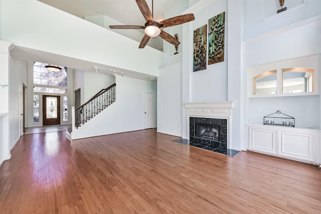 unfurnished living room with ceiling fan, a high ceiling, a premium fireplace, wood finished floors, and stairs