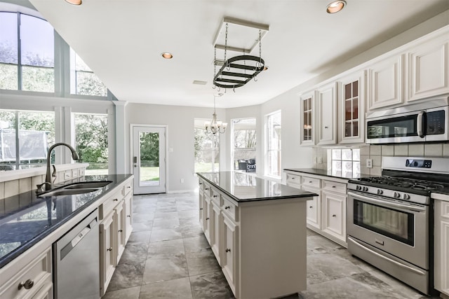 kitchen with dark countertops, glass insert cabinets, an inviting chandelier, stainless steel appliances, and a sink