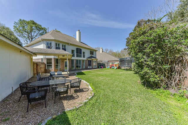 rear view of house featuring a shingled roof, a patio, a trampoline, fence, and a yard