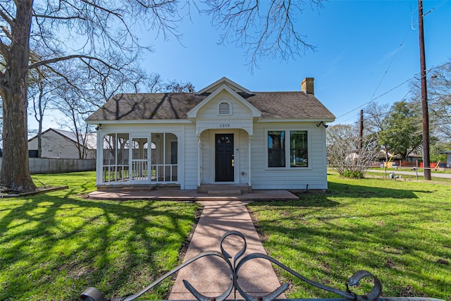 view of front of property with roof with shingles, a front lawn, a chimney, and fence