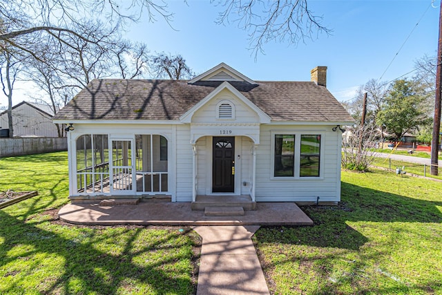 view of front facade with a shingled roof, a sunroom, a chimney, fence, and a front yard