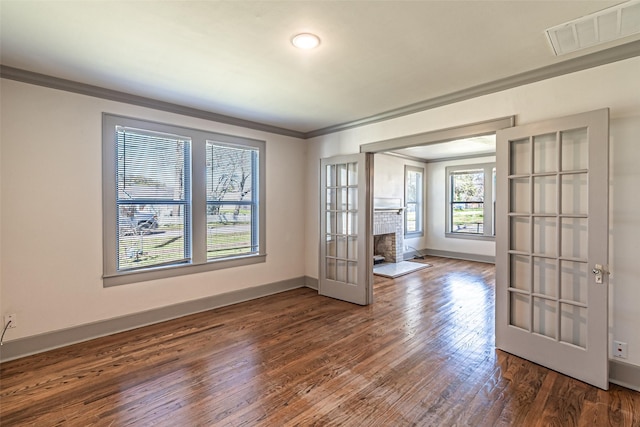 empty room featuring hardwood / wood-style flooring, visible vents, baseboards, a brick fireplace, and crown molding