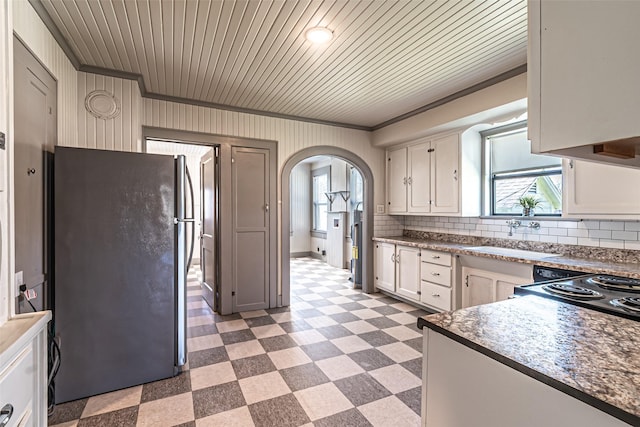 kitchen featuring arched walkways, crown molding, light floors, freestanding refrigerator, and a sink