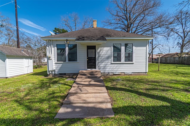 bungalow-style house with a chimney, a shingled roof, fence, an outdoor structure, and a front lawn