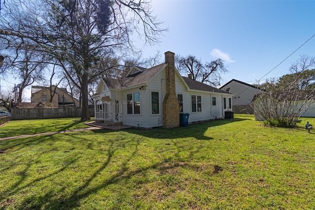 rear view of property with a yard, central AC, fence, and a chimney