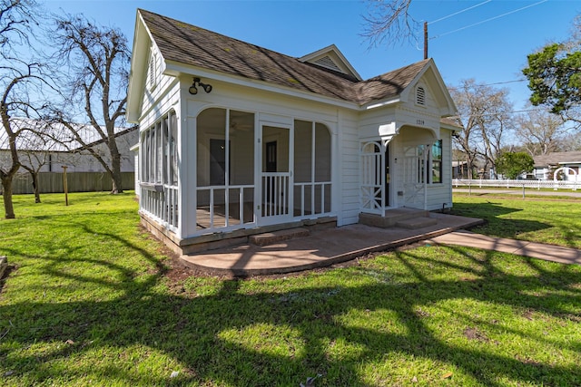 rear view of property with a shingled roof, a sunroom, fence, and a lawn