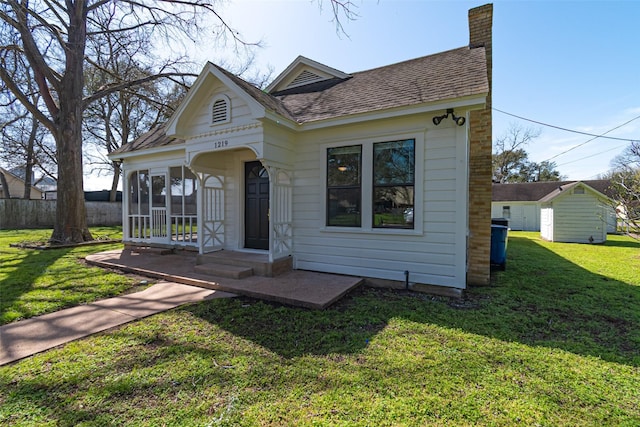 view of front facade featuring a sunroom, a shingled roof, a chimney, and a front lawn