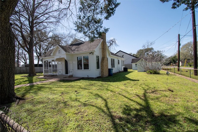 view of front facade with an outbuilding, a front lawn, a chimney, and a fenced backyard