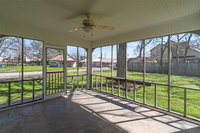 unfurnished sunroom featuring ceiling fan and a residential view