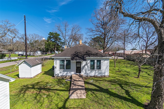 bungalow-style house featuring a front yard, roof with shingles, an outdoor structure, and a storage unit