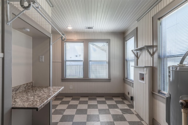 interior space with laundry area, visible vents, dark floors, wood walls, and water heater