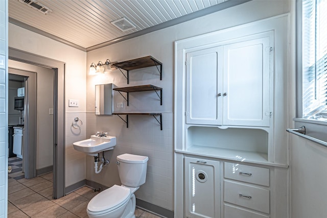 half bathroom featuring toilet, tile patterned flooring, visible vents, and tile walls