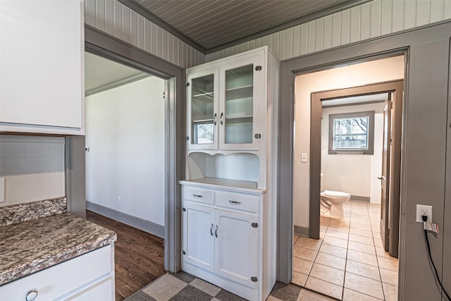 kitchen featuring glass insert cabinets, white cabinetry, backsplash, and baseboards