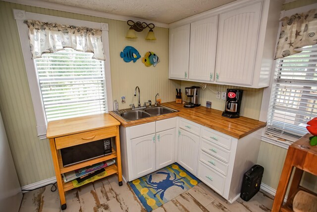 kitchen with a textured ceiling, butcher block countertops, a sink, and white cabinetry