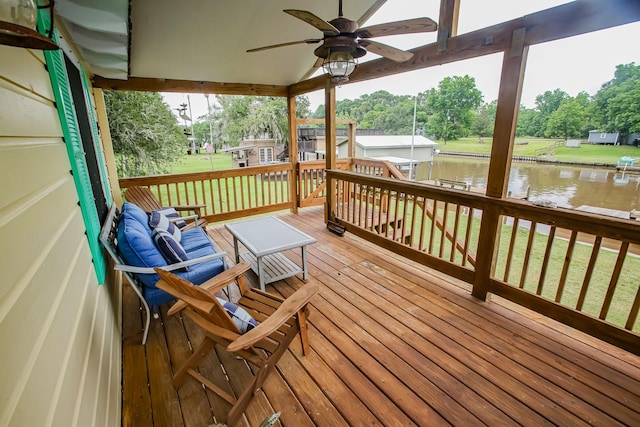 wooden deck with a water view, ceiling fan, and a lawn