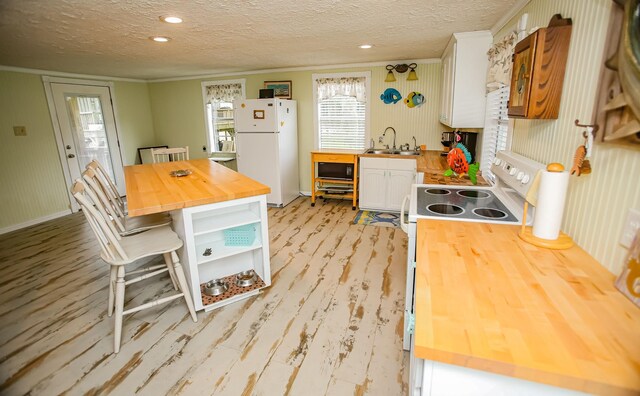 kitchen with butcher block counters, a sink, freestanding refrigerator, and white cabinetry