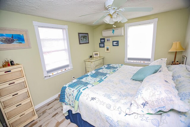 bedroom featuring light wood-style floors, ceiling fan, a textured ceiling, a wall mounted air conditioner, and baseboards