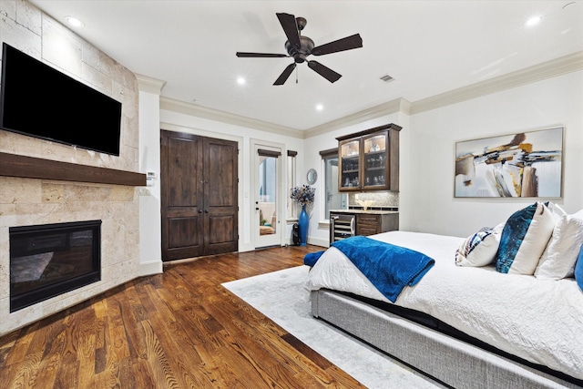 bedroom featuring visible vents, dark wood finished floors, crown molding, and a tile fireplace