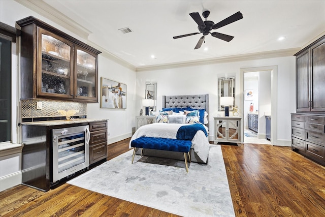 bedroom with wine cooler, dark wood-type flooring, visible vents, a bar, and crown molding