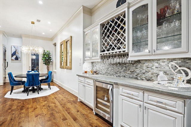 bar with beverage cooler, ornamental molding, backsplash, a dry bar, and decorative light fixtures