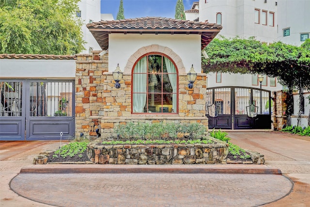 property entrance with stucco siding, a gate, stone siding, and a tiled roof