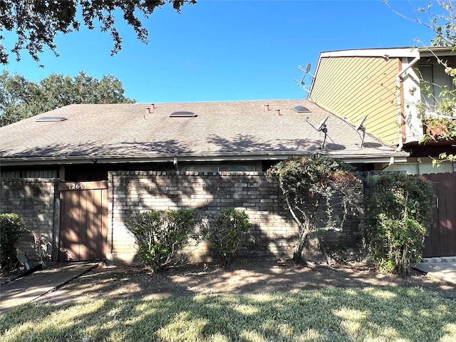 back of property with roof with shingles, fence, and brick siding