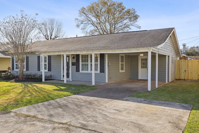 ranch-style home featuring concrete driveway, roof with shingles, fence, a front lawn, and a carport