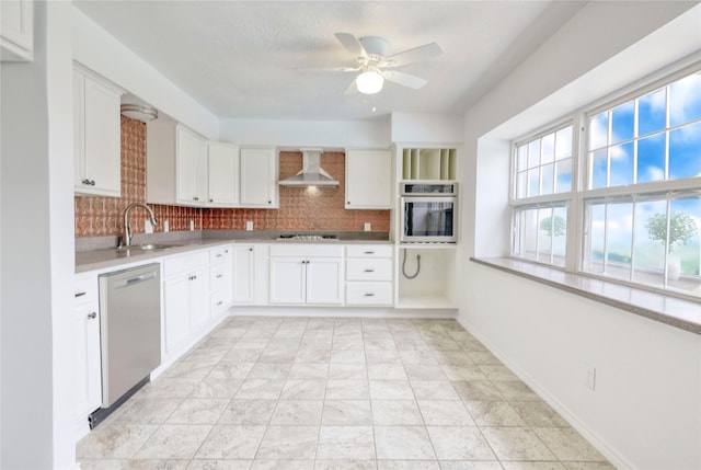 kitchen featuring stainless steel appliances, a sink, light countertops, wall chimney range hood, and decorative backsplash