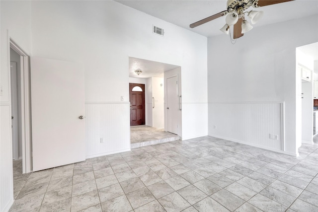 empty room with ceiling fan, visible vents, and wainscoting