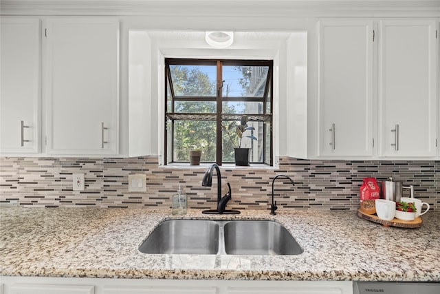 kitchen featuring light stone counters, white cabinets, a sink, and decorative backsplash