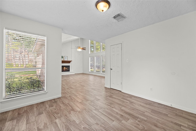 spare room with visible vents, a ceiling fan, a lit fireplace, a textured ceiling, and light wood-style floors