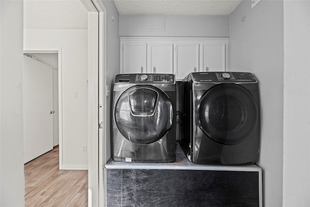 clothes washing area with a textured ceiling, wood finished floors, baseboards, independent washer and dryer, and cabinet space