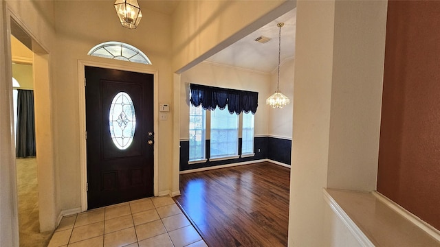 foyer entrance with a chandelier, wood finished floors, visible vents, vaulted ceiling, and ornamental molding