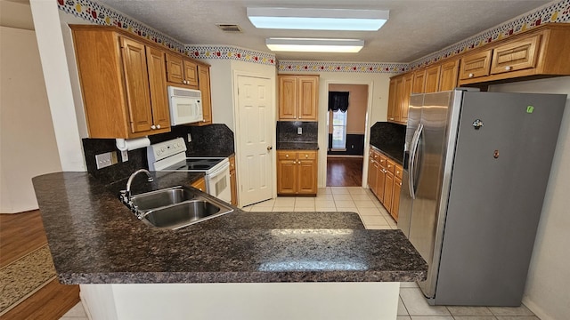 kitchen featuring a peninsula, white appliances, a sink, visible vents, and backsplash