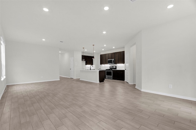 unfurnished living room featuring baseboards, recessed lighting, light wood-type flooring, and a sink