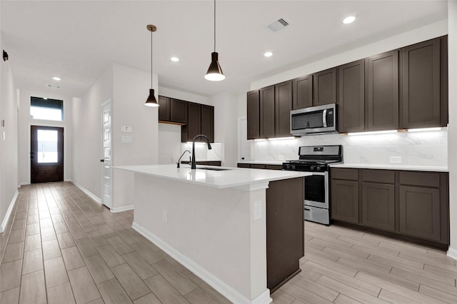 kitchen featuring an island with sink, a sink, backsplash, appliances with stainless steel finishes, and wood tiled floor