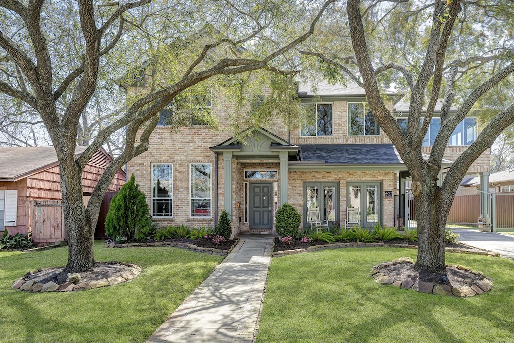 view of front of home featuring a shingled roof, a front yard, fence, and brick siding