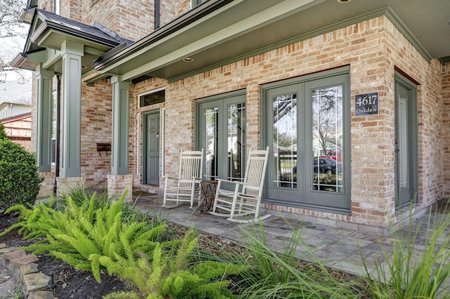 property entrance with brick siding, a porch, and french doors