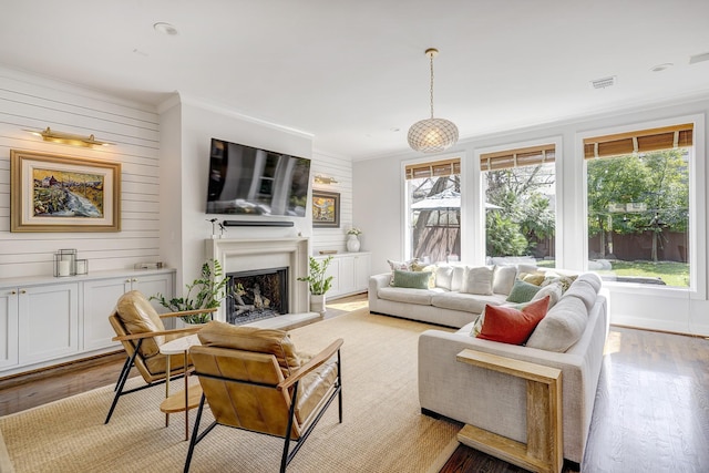 living area featuring a fireplace with raised hearth, wood walls, visible vents, light wood-style floors, and ornamental molding