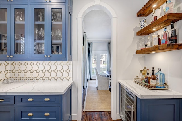 bar featuring a dry bar, beverage cooler, tasteful backsplash, arched walkways, and dark wood finished floors