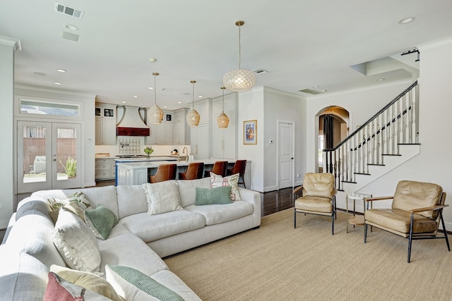 living room with arched walkways, visible vents, crown molding, and stairway