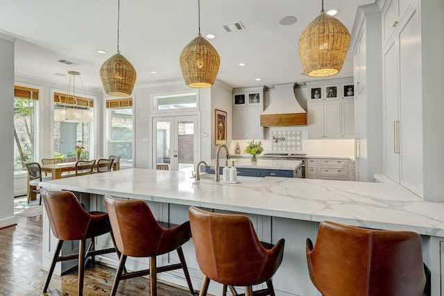 kitchen featuring french doors, tasteful backsplash, custom range hood, visible vents, and a sink