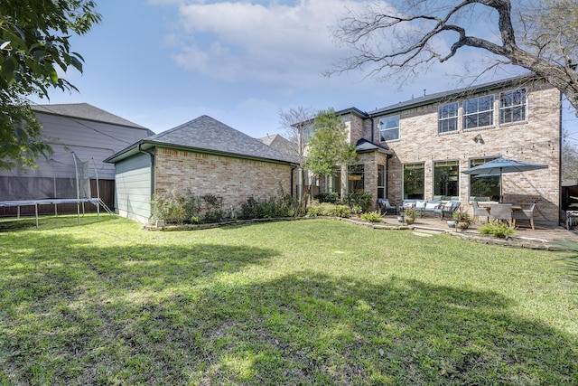 rear view of house with a yard, brick siding, a trampoline, and a patio area