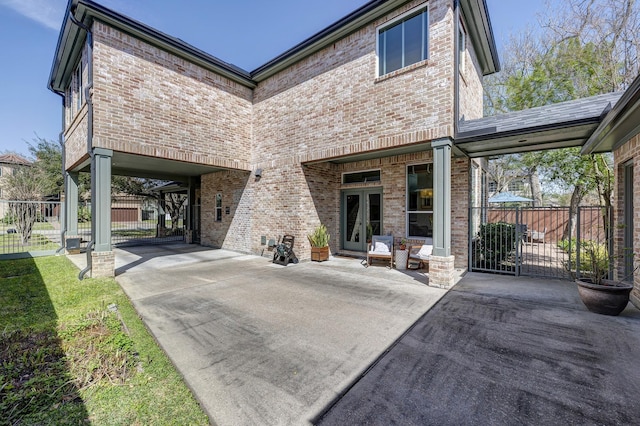 rear view of house with french doors, fence, brick siding, and a gate