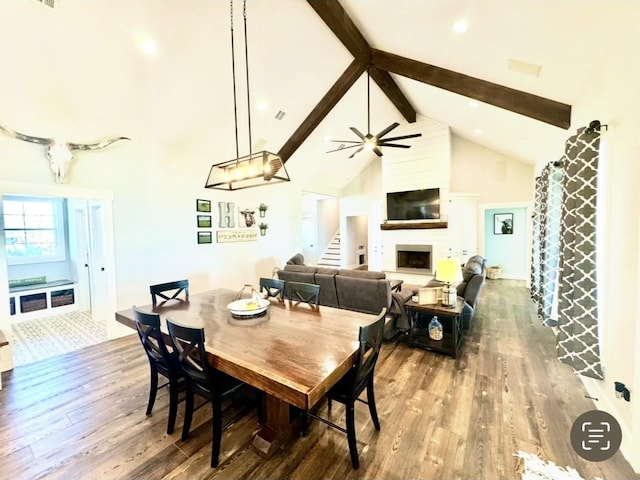 dining space with high vaulted ceiling, a large fireplace, wood finished floors, stairway, and beamed ceiling