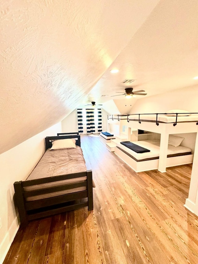 bedroom with baseboards, visible vents, lofted ceiling, wood finished floors, and a textured ceiling